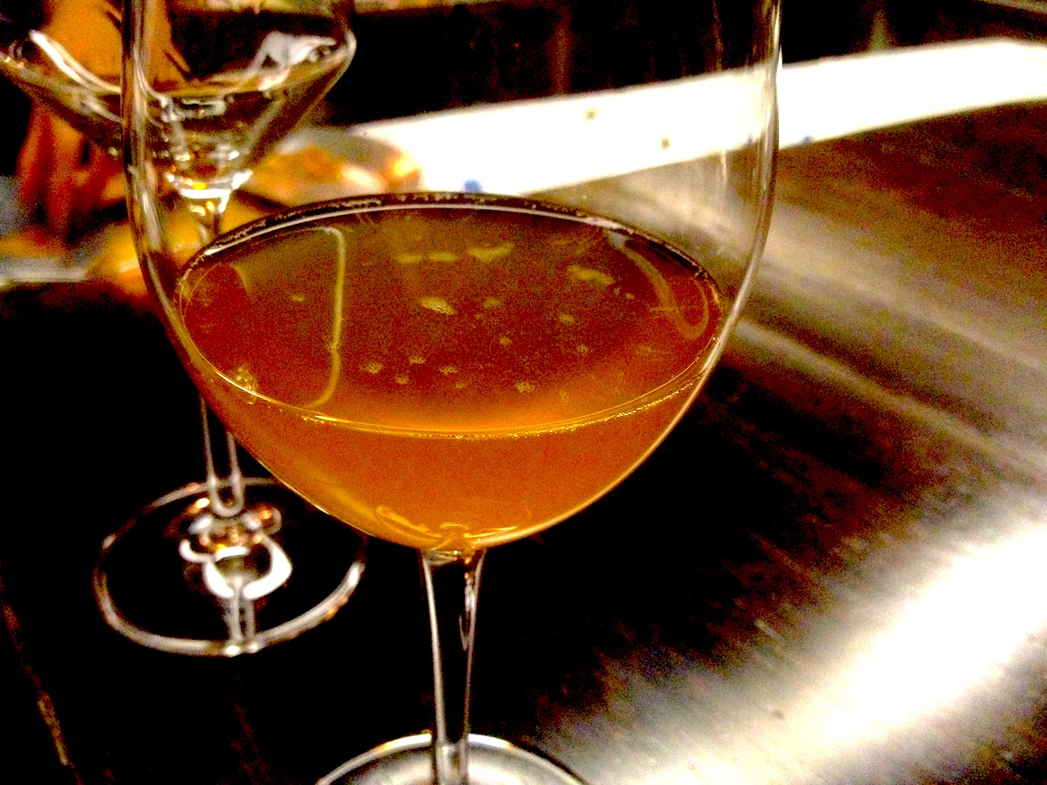 a glass of orange wine on a dark wood counter