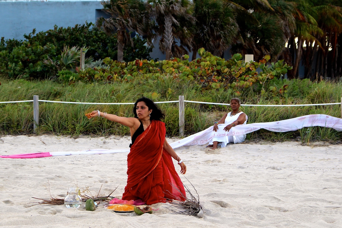 woman in red sari kneeling in the sand