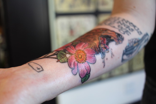 A white arm with a tattoo of a bear and a pink flower