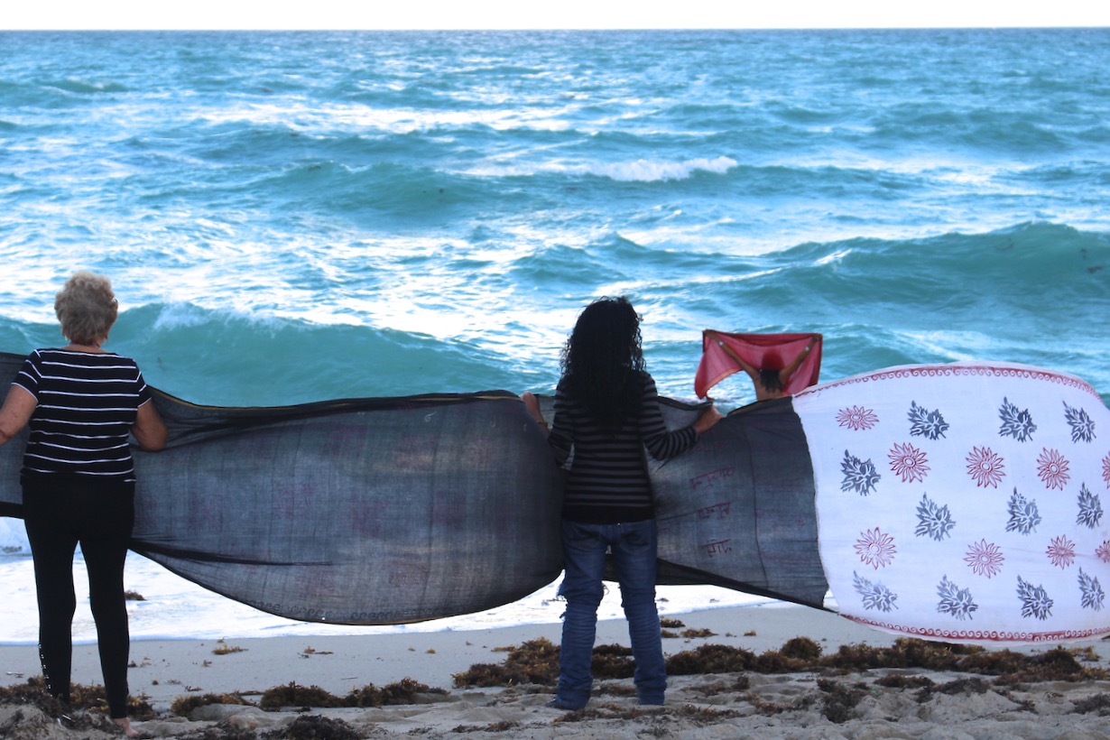 Women holding a lenth of sari, facing the ocean